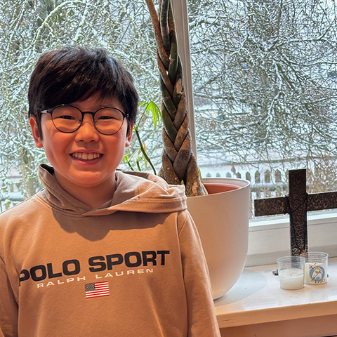 Manuel vor Fenster mit Kreuz und Kerzen mit verschneitem Garten im Hintergrund