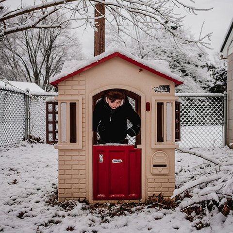 Beiges Spielhaus mit roter Tür und Kind in verschneitem Garten