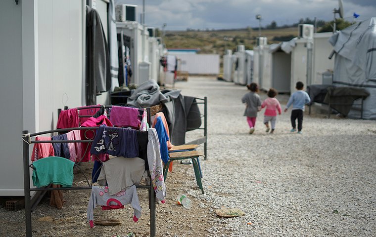 Flüchtlingscamp mit bunter Kinderkleidung auf Stühlen und drei kleinen Kindern