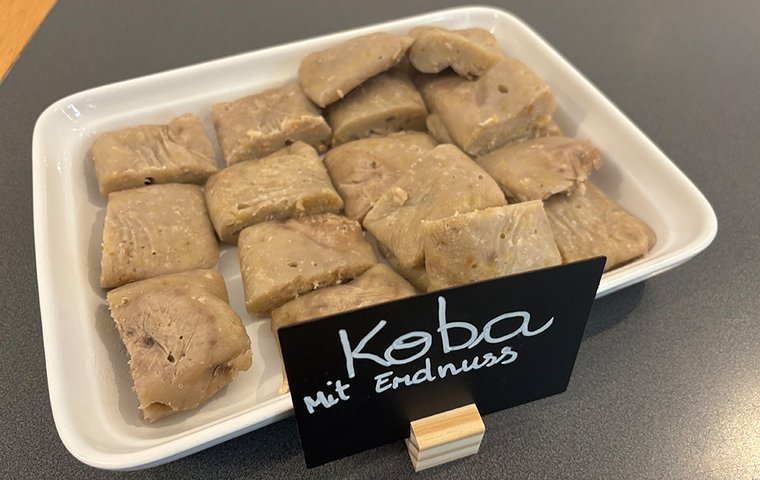 Platte mit eckigen Koba-Stücken und Schild "Koba mit Erdnüssen"