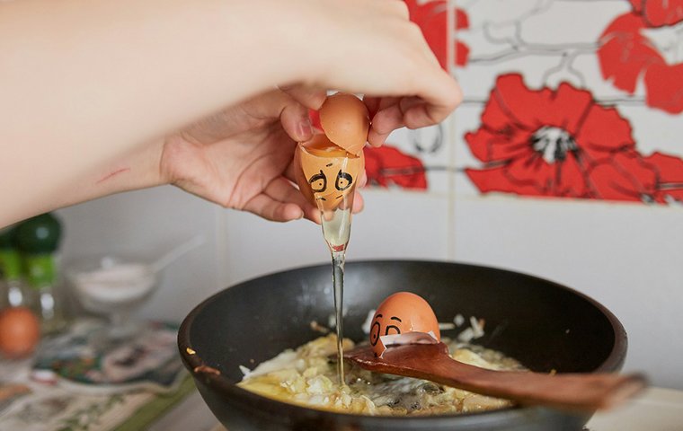 Eier mit aufgemalten Gesichtern werden in Pfanne geschlagen.