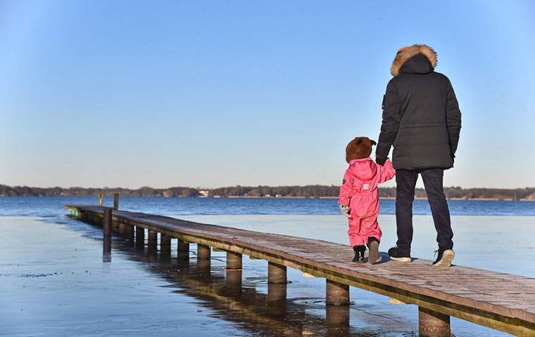 Vater mit Kind gehen auf Holzsteg am See.